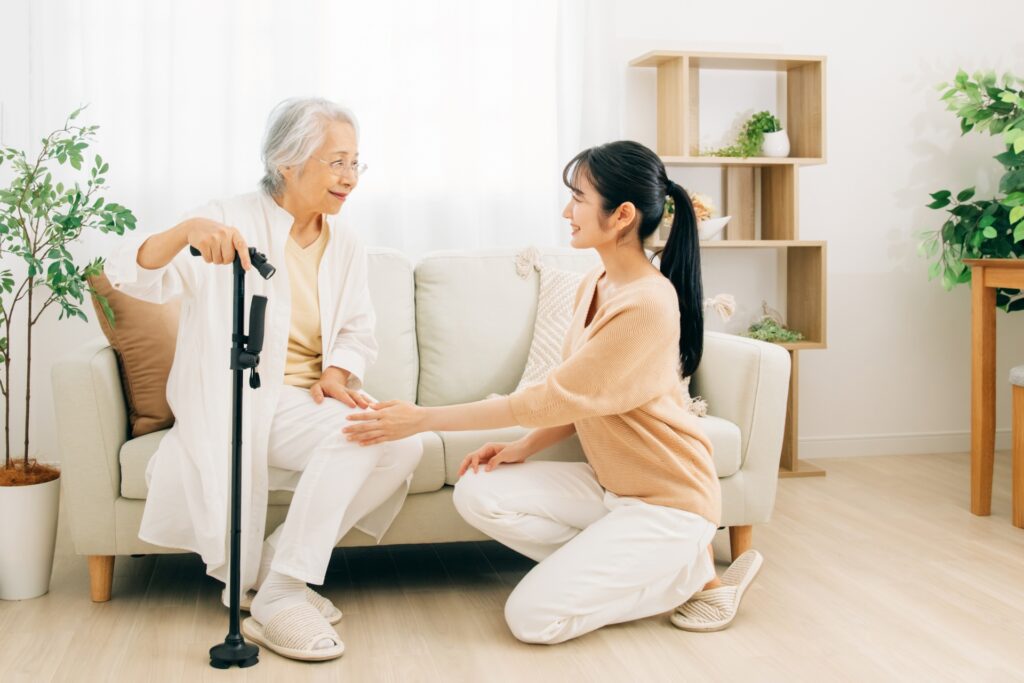 ソファに座る高齢の母親に、しゃがんで目線を合わせて語りかける娘。そばに多点杖