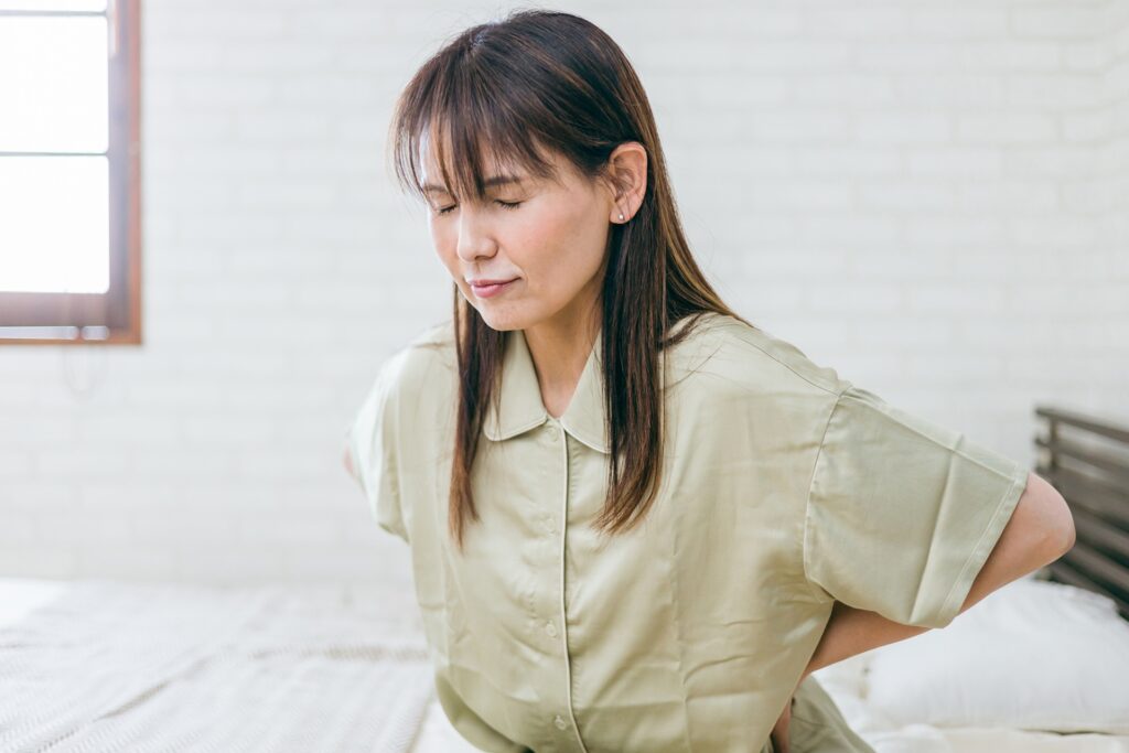 朝、ベッドの端に座って腰に手を当てる女性