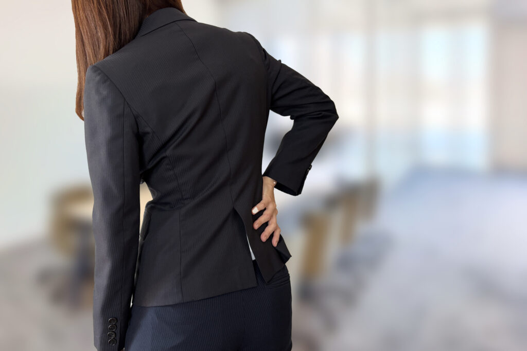 腰に手を当てて痛みをこらえるスーツ姿の女性
